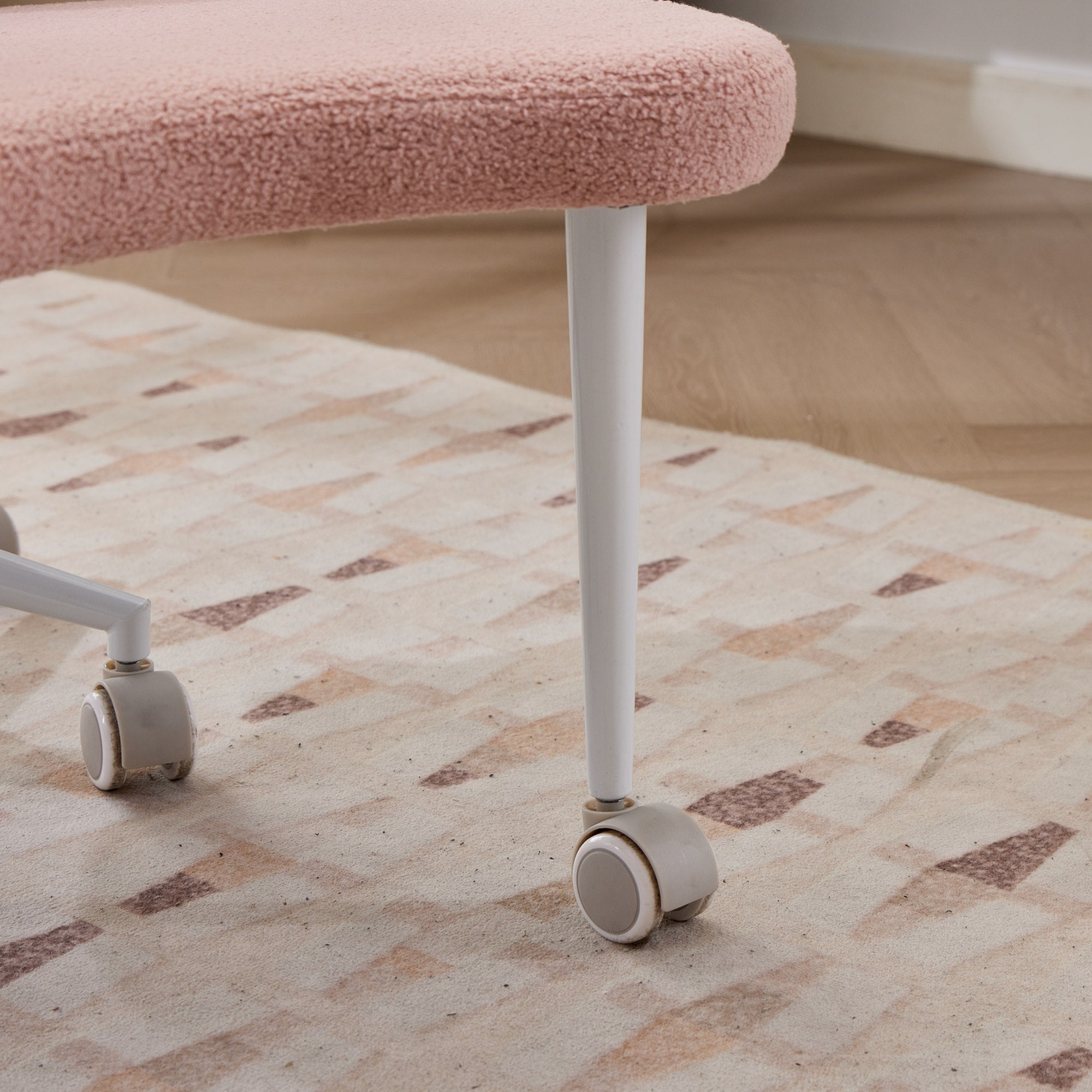 Pink cushioned cross-legged meditation chair with white metal legs and caster wheels on a beige rug.