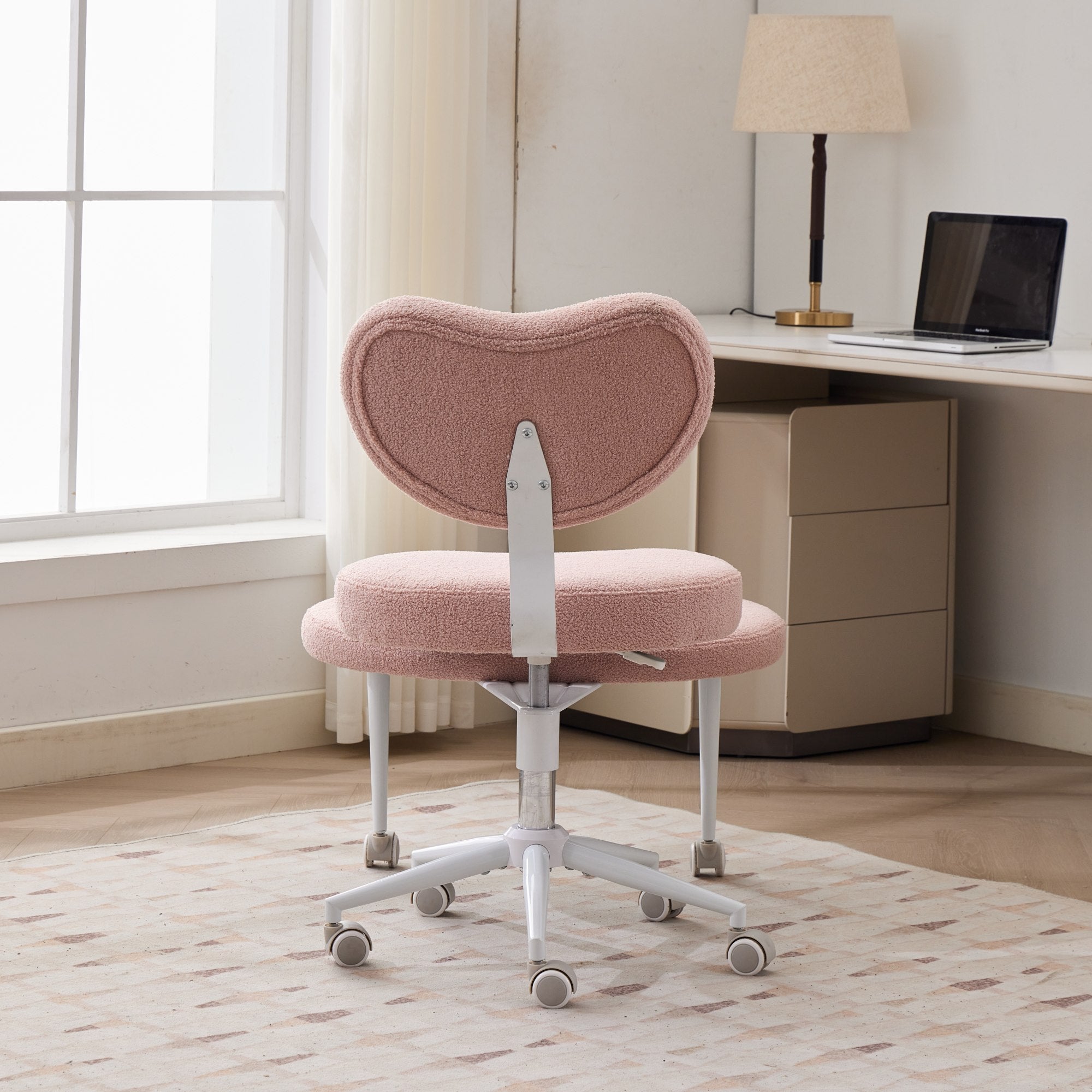Pink cross-legged meditation chair with wheels and lumbar support in a bright home office.