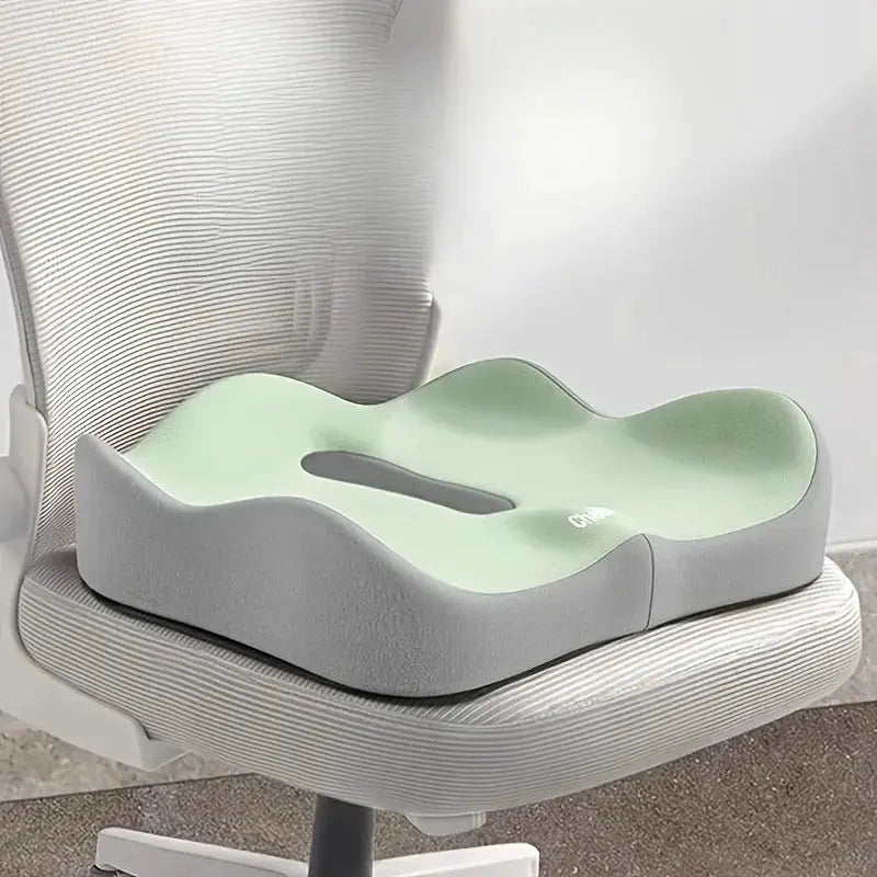 Ergonomic memory foam seat cushion with lumbar support for posture on an office chair, light green top and gray sides.