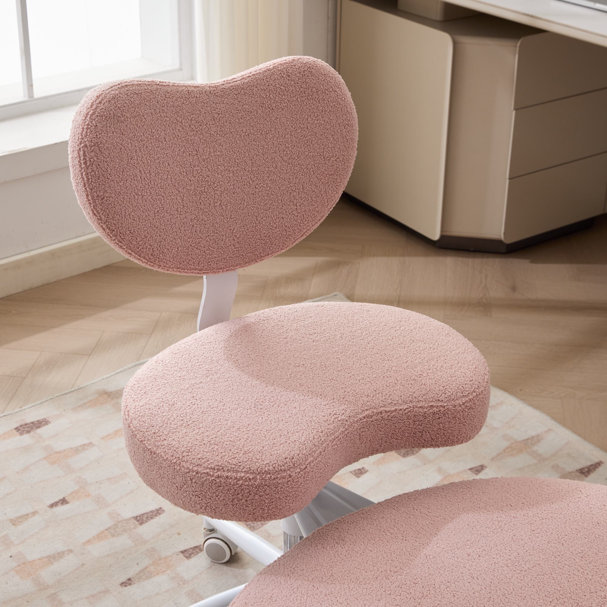 Pink fuzzy cross-legged meditation chair on wheels with lumbar support in a home office.